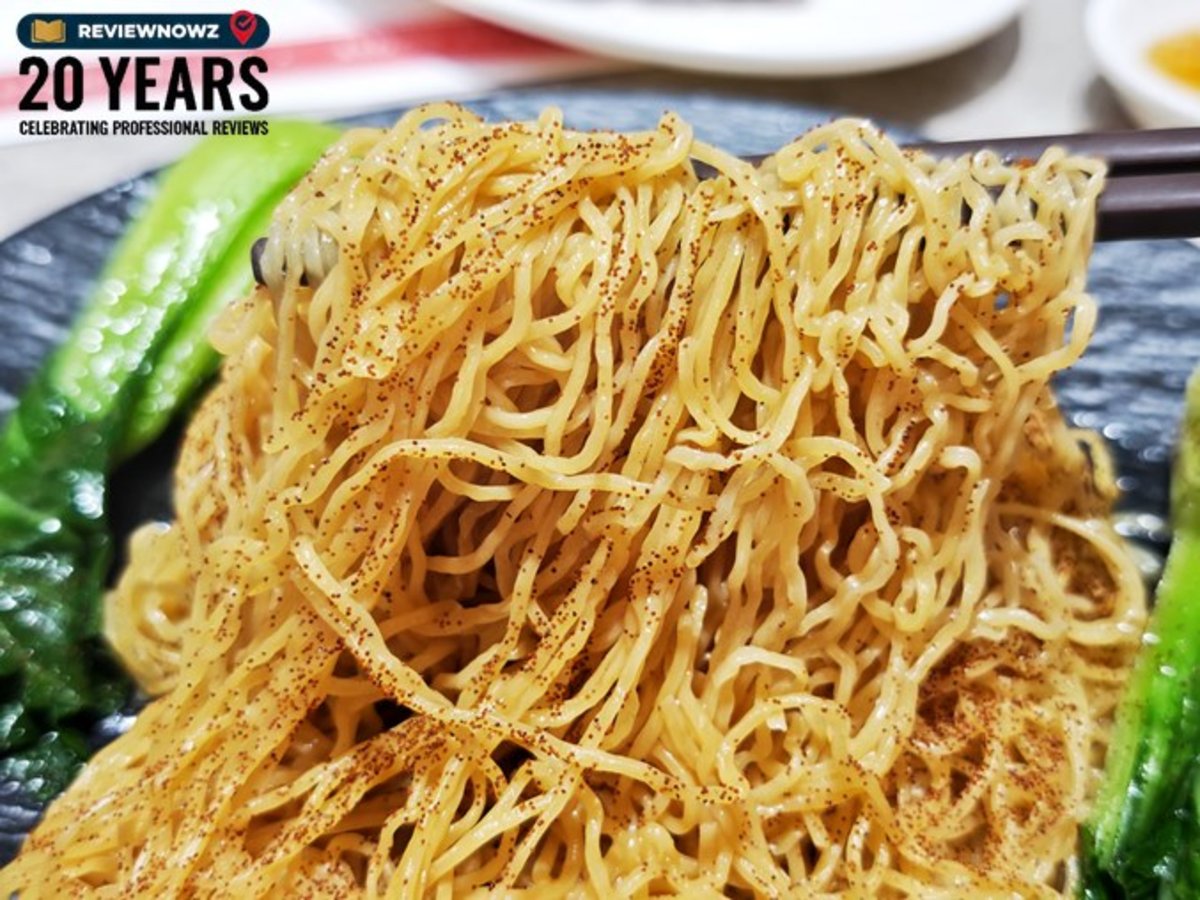 ตะเกียบคีบเส้นบะหมี่แห้งคลุกไข่กุ้งสีส้มละเอียด โชว์ความเหนียวนุ่มน่าทาน เคียงด้วยผักกวางตุ้งฮ่องกง ในโปรโมชั่นราคาพิเศษ 99 บาท ที่ร้าน Kam's Roast Thailand