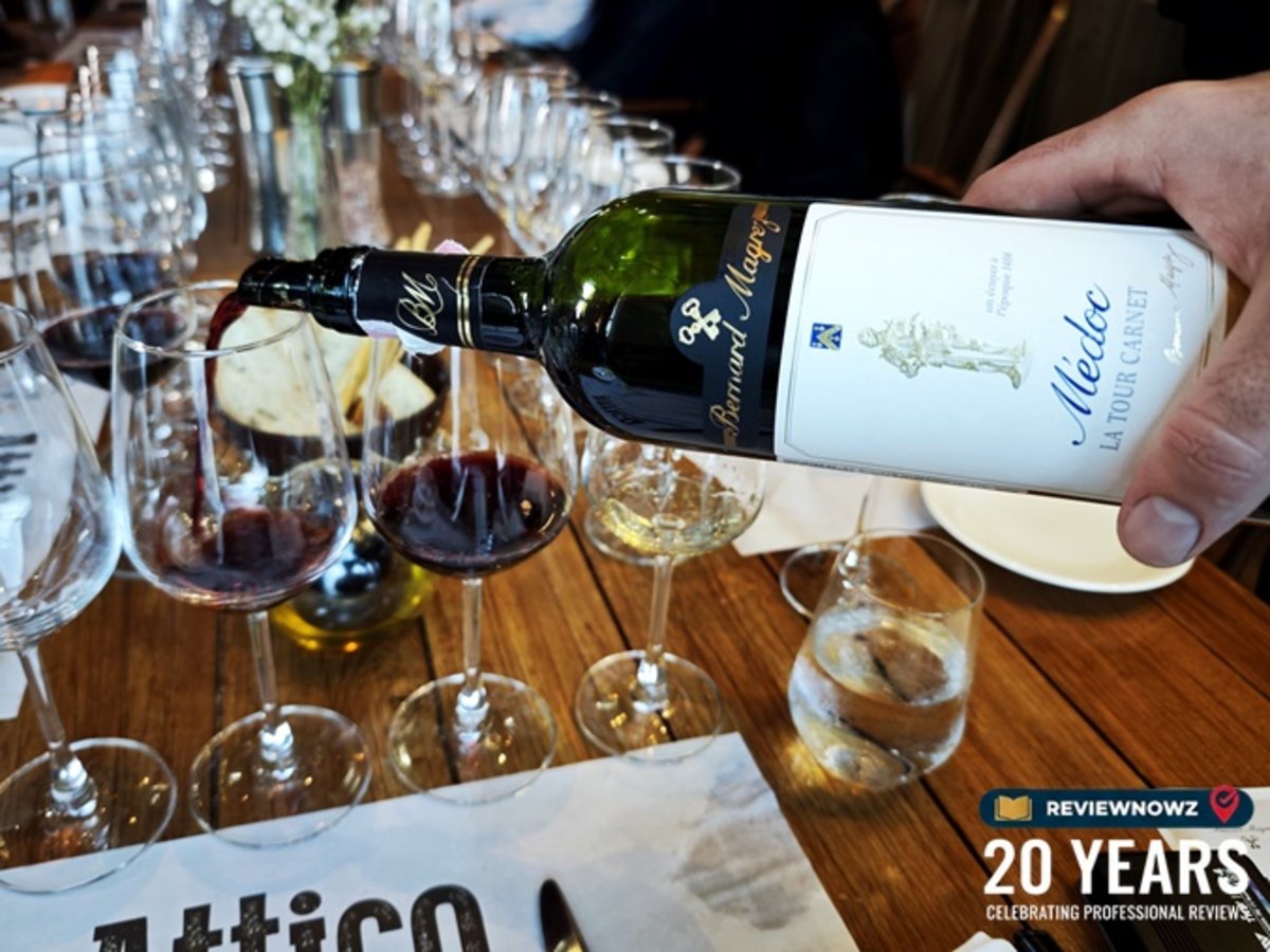 การรินไวน์แดง Médoc de La Tour Carnet, Médoc, 2021 จากขวดแก้วสีเข้มลงในแก้วไวน์คริสตัลทรงสูงอย่างประณีต บนขวดเผยให้เห็นฉลากสีขาวที่มีรูปอัศวินสีทองและตราสัญลักษณ์ลูกกุญแจคู่ไขว้ของ Bernard Magrez อย่างชัดเจน ท่ามกลางบรรยากาศงาน Bordeaux Wine Masterclasses ณ ห้องอาหาร Attico โรงแรม Radisson Blu Plaza Bangkok
