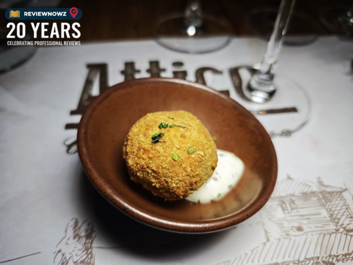 เมนู Pulled beef croquette โครเก็ตเนื้อวัวฉีกทรงกลมชิ้นใหญ่ทอดกรอบสีเหลืองทอง โรยหน้าด้วยสมุนไพรสดสับ เสิร์ฟพร้อมซอสทรัฟเฟิลมายองเนสในถ้วยดินเผาสีน้ำตาล จัดวางบนกระดาษรองจานลายเส้นสำหรับงานรีวิวอาหาร ณ ห้องอาหาร Attico โรงแรม Radisson Blu Plaza Bangkok
