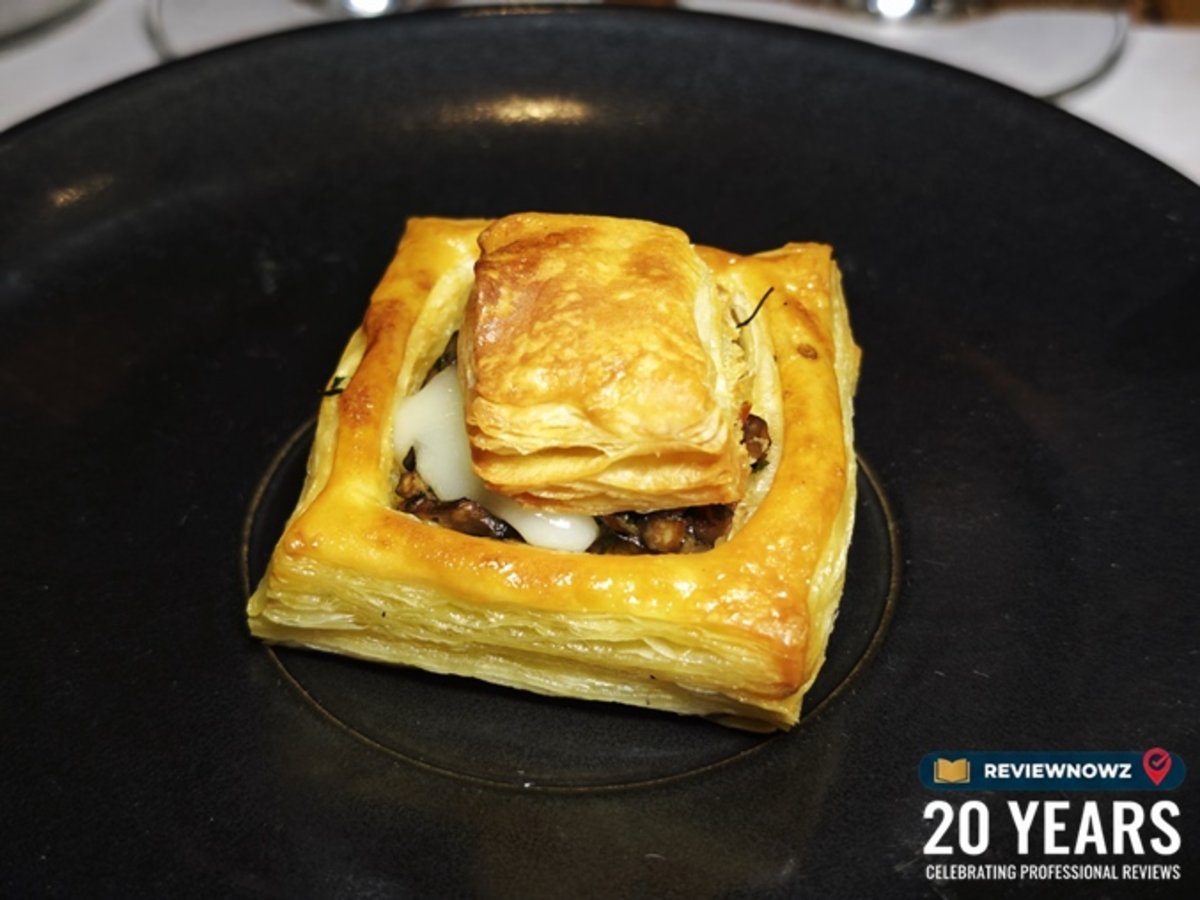 เมนูคาว Mushroom and taleggio millefeuille พายมิลเฟยอบกรอบสีเหลืองทองสอดไส้เห็ดและทาเลจจิโอชีสเยิ้ม จัดวางอย่างประณีตตรงกลางจานสีดำสนิท สำหรับงานรีวิวอาหาร ณ ห้องอาหาร Attico โรงแรม Radisson Blu Plaza Bangkok